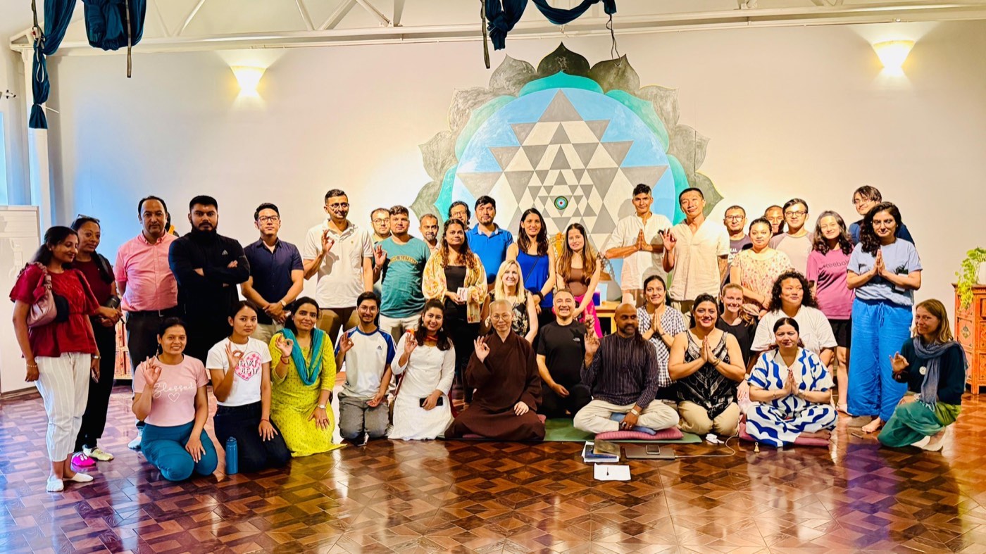 A large group of people smiling with hands in prayer pose after a singing circle