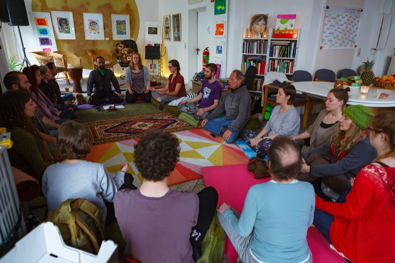 A group meditating together in a circle on mats and cushions