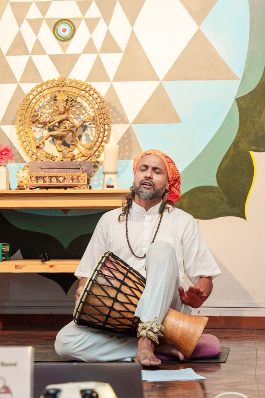 Anup playing a hand drum and singing in a meditation hall