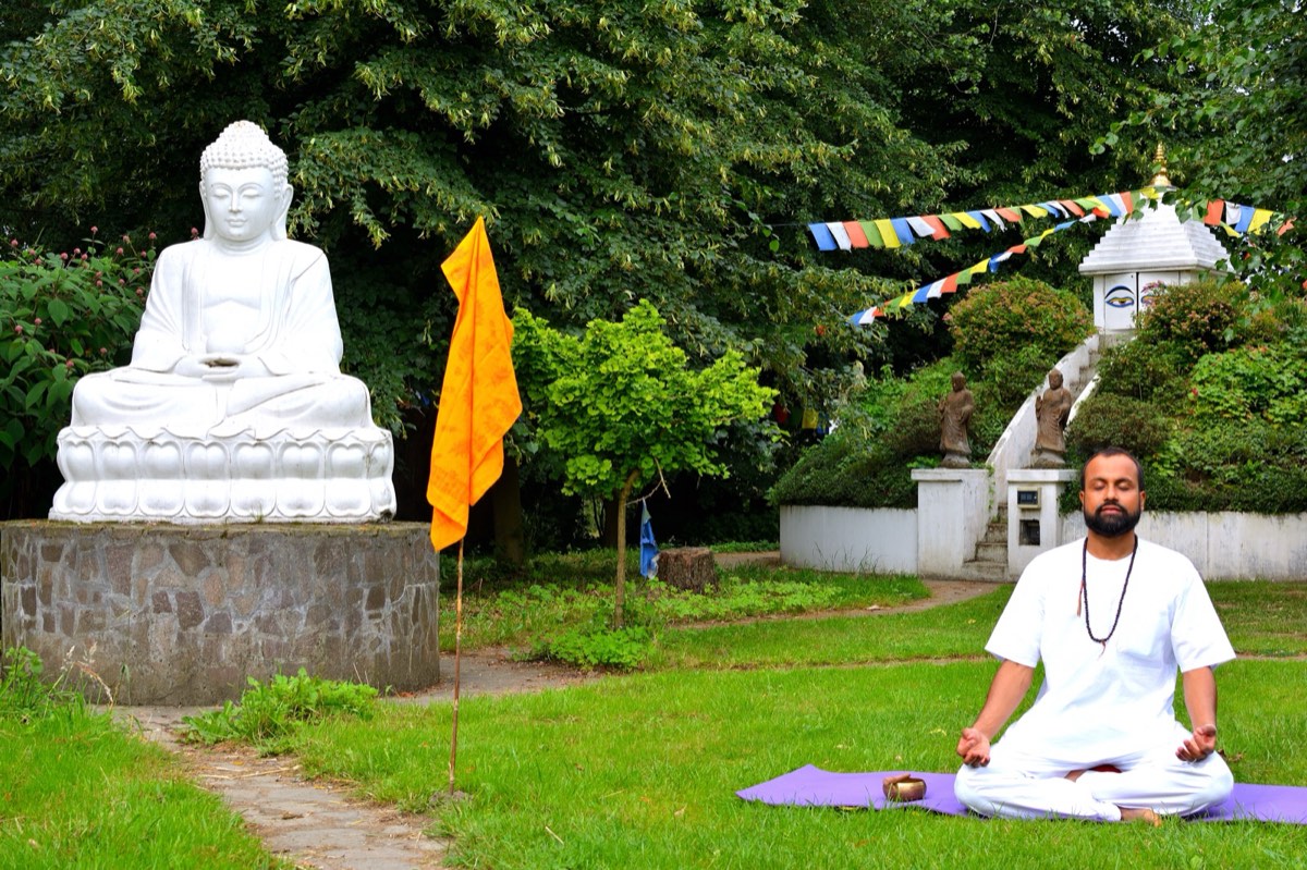 Anup meditating in a garden in front of a white Buddha statue